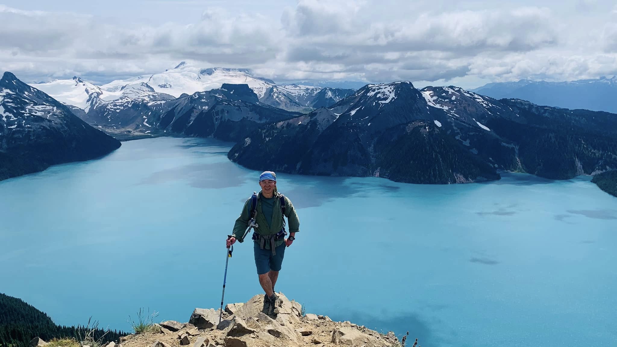 Hiker overlooking turquoise Garibaldi Lake with snow-capped mountains in British Columbia